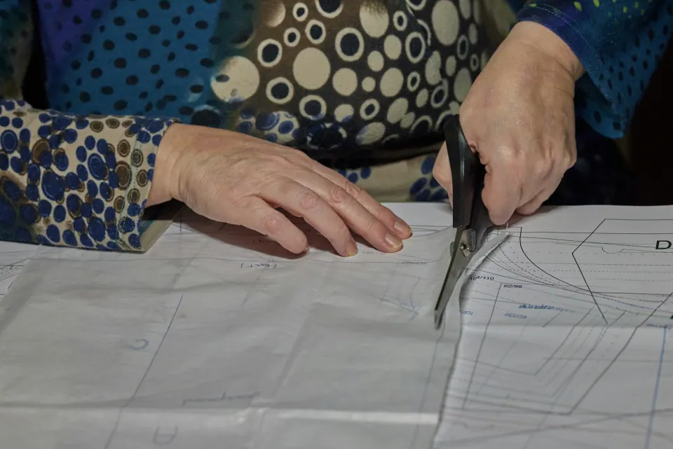 Hands cutting a paper garment pattern with shears