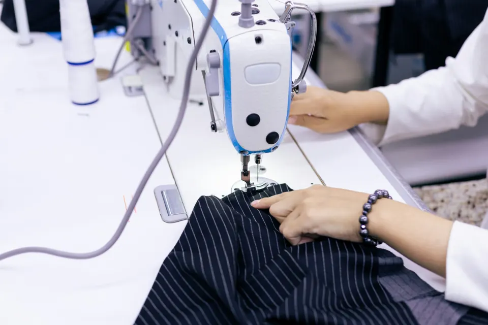 Hands guiding pinstripe suit fabric through an industrial sewing machine
