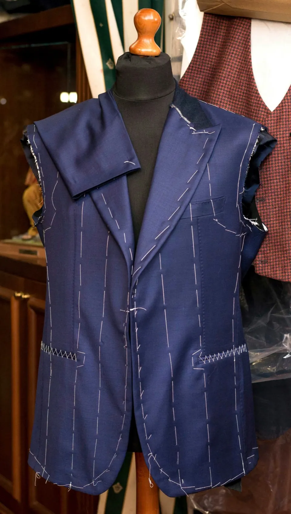 Basted navy suit jacket with white tacking stitches on a dress form