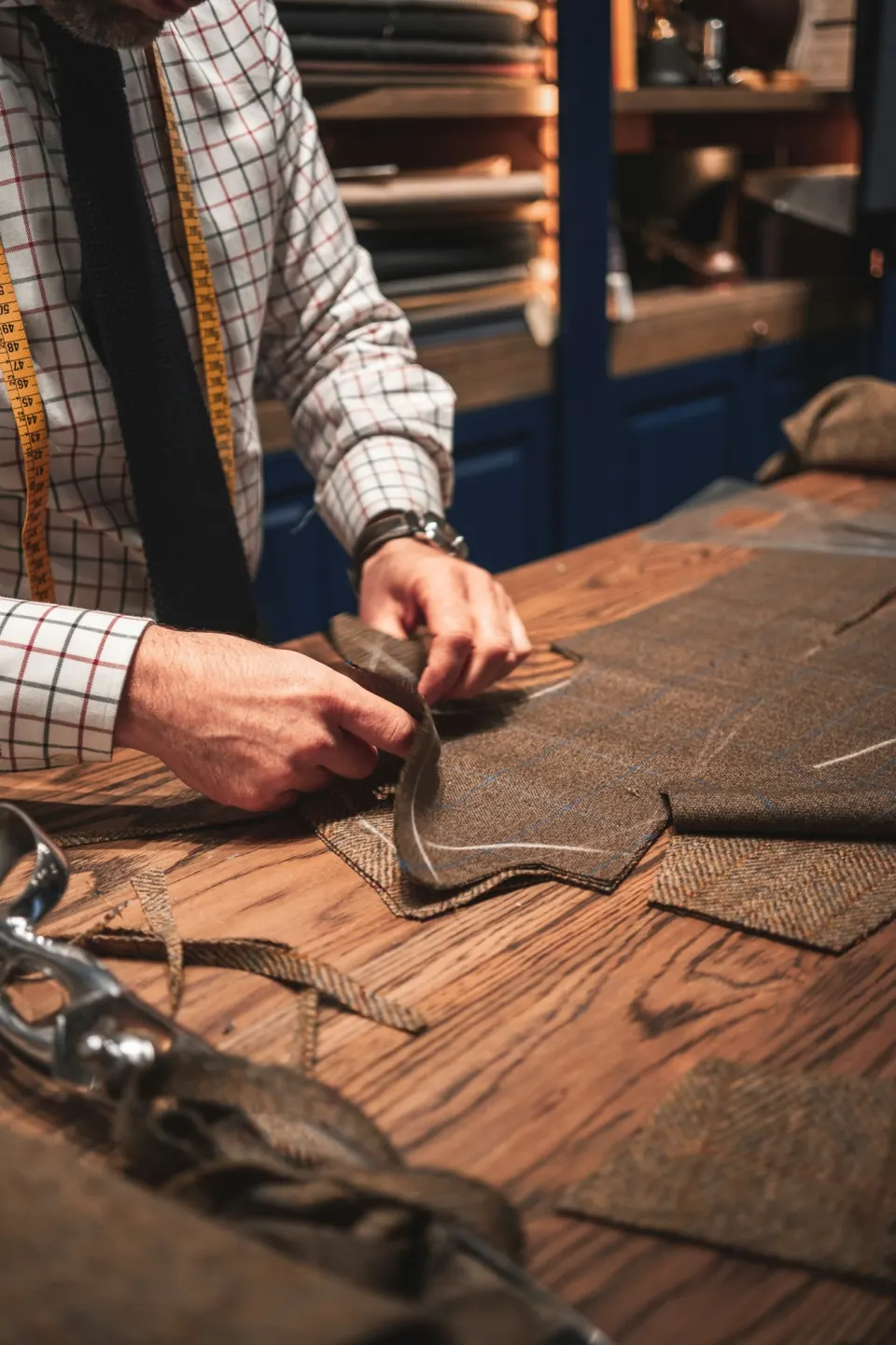 Tailor's hands cutting chalk-marked tweed suit panels on a workbench