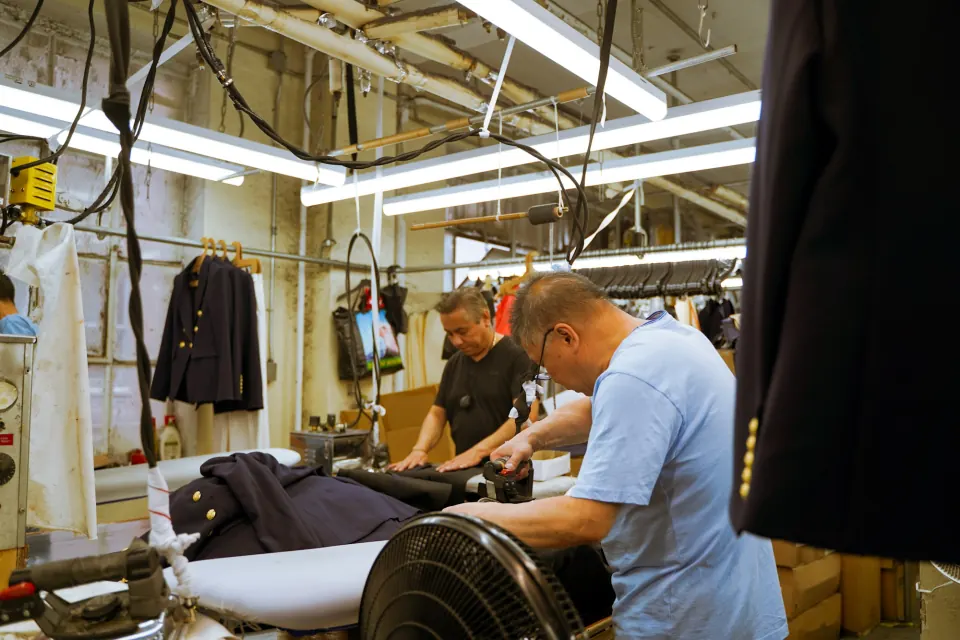 Pressers working on navy tailored jackets in a garment workshop