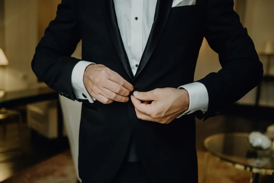 Hands buttoning a black shawl-lapel tuxedo jacket